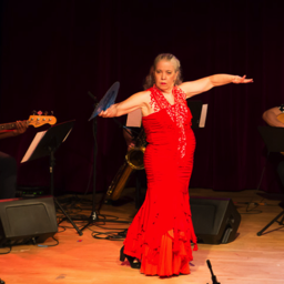 Aurora Reyes, red sleeveless flamenco dress, arms extended side to side, 3 musicians in background.
