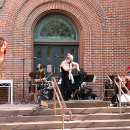 Image: left-right, Omar Edwards, orange short sleeved shirt and shorts, Aurora Reyes, black costume and black and white polka dot flamenco scarf,and  dancing Sevillanas Afro Cubanas at JPAC 8.21.20. Accompanied by Zach O'Farrill, drums, Danny Rivera, baritone saxophone and Basilio Georges, guitar, photo: Eric Bandiero